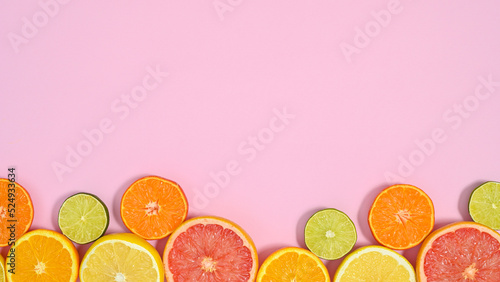 Sliced citrus fruits on bottom of pastel pink background with copy space. Flat lay