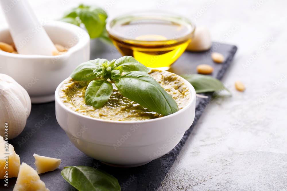 Pesto sauce and ingredients, black cheese board, basil, garlic, pine nuts, olive oil on grey stone background with copy space Pesto sauce and ingredients, black cheese board, basil, garlic, pine nuts, olive oil on grey stone background with copy space