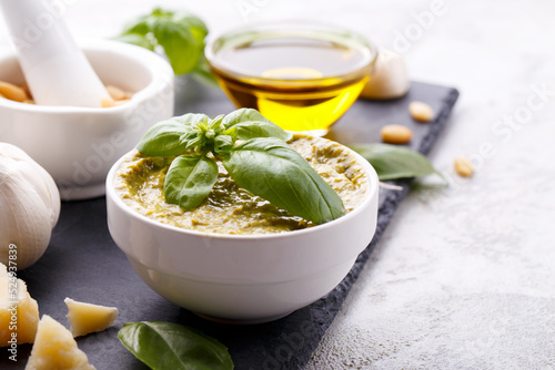 Pesto sauce and ingredients, black cheese board, basil, garlic, pine nuts, olive oil on grey stone background with copy space
