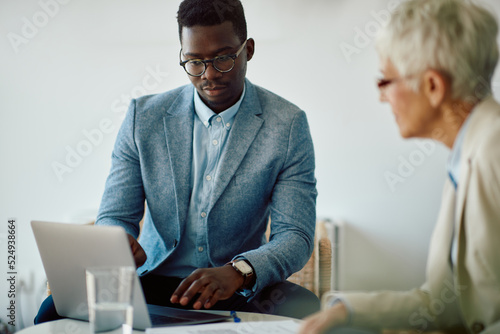 Young black businessman using computer during meeting with female colleague in office.