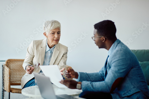 Senior businesswoman and her young her colleague talk while going through paperwork in office. photo