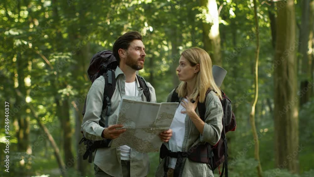 Emotional man and woman tourists getting lost in forest, arguing with map, feeling disagree, go in different directions Emotional man and woman tourists getting lost in forest, arguing with map, feeling disagree, go in different directions