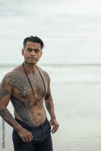 Handsome tanned tattooed sexy man with a naked torso in a flying poreo on the ocean at sunset.