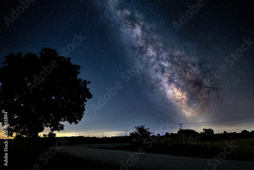Night sky with Milky way over the landscape and Asphalt road in the countryside go in the same direction.