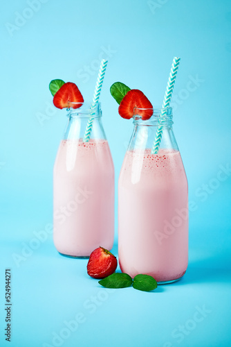 Strawberry smoothie or milkshake in glass jar with berries on blue background. Healthy summer drink