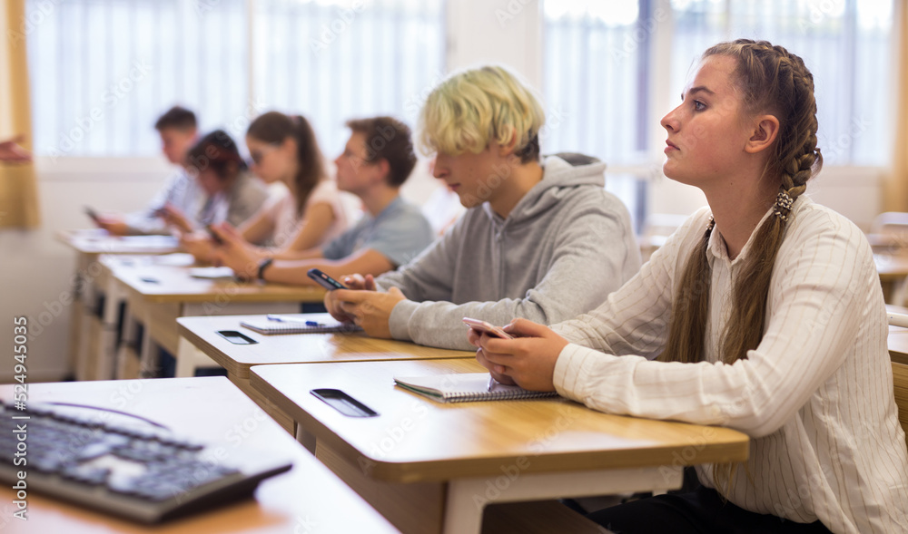 Confident teen students using social media on phones while studying in high school