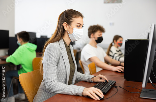 Concentrated young woman in protective mask studying in computer lab in public library during coronavirus pandemic..