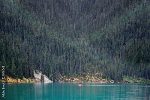 Fototapeta Naklejka Na Ścianę i Meble -  People in tiny canoe on turquoise blue lake with forest in the background