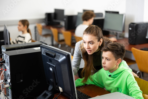 Woman teacher helps guy with learning on computer in school class
