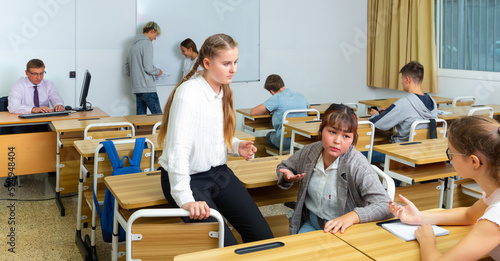 Cheerful teenage girls classmates communicating in classroom during break between lessons in college