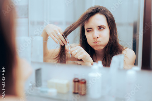 Puzzled Woman Trying to Cut her Bangs in the Mirror. Girl having a do-it-yourself haircut in the bathroom, at home
