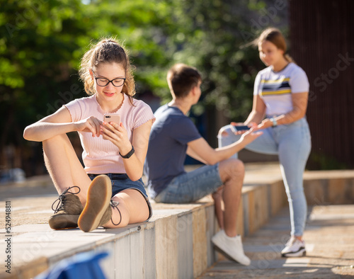 Portrait of cute teen girl carried away with smartphone outdoor on summer day