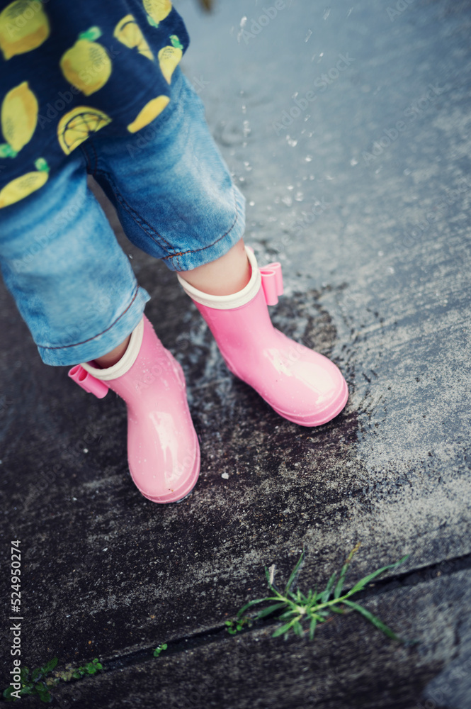 梅雨の雨の日に長靴を履いて水たまりで遊ぶ子ども