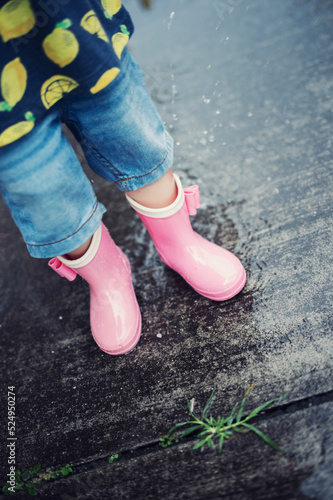 梅雨の雨の日に長靴を履いて水たまりで遊ぶ子ども