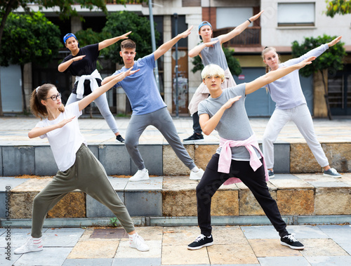 Group of modern teenagers performing street dance choreography outdoors in summer.