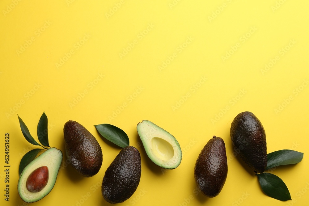 Whole and cut ripe avocadoes with green leaves on yellow background, flat lay. Space for text Whole and cut ripe avocadoes with green leaves on yellow background, flat lay. Space for text