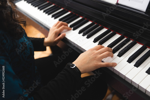 Close up of woman s hands playing piano by reading sheet music. Selective focus