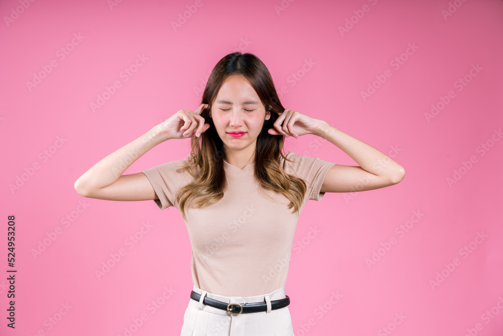 Asian woman finger covering your ear to mute loud noise her unhappy sound expression on the pink background Asian woman finger covering your ear to mute loud noise her unhappy sound expression on the pink background