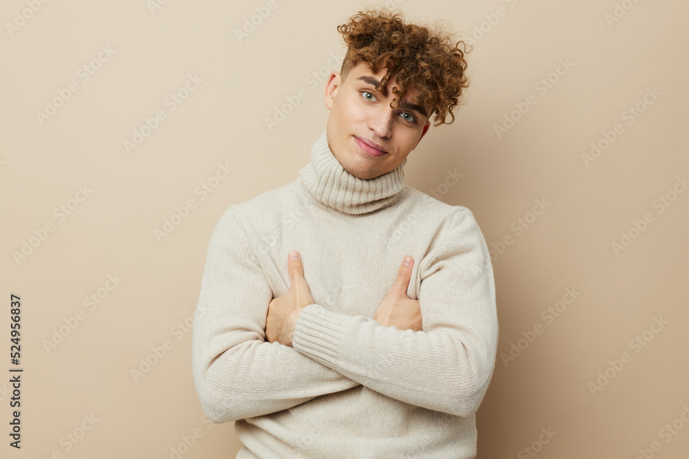 a handsome attractive man stands on a beige background in a light turtleneck and keeps his arms crossed on his chest a handsome attractive man stands on a beige background in a light turtleneck and keeps his arms crossed on his chest