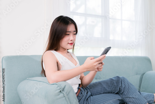 Asian woman use mobile phone her enjoy and fun sitting on sofa in living room at home