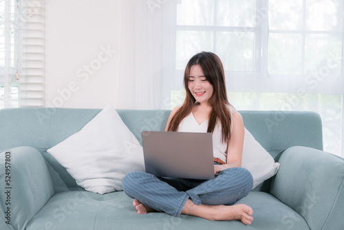 Asian woman use laptop computer her enjoy and fun sitting on sofa in living room at home