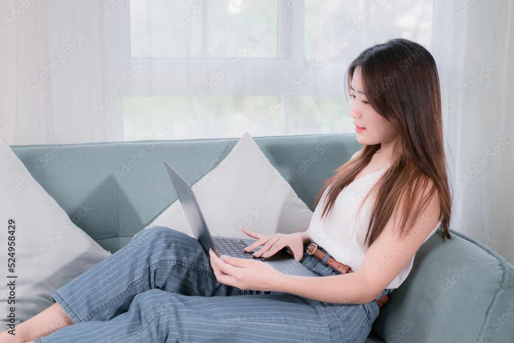 Asian woman use laptop computer her enjoy and fun sitting on sofa in living room at home Asian woman use laptop computer her enjoy and fun sitting on sofa in living room at home