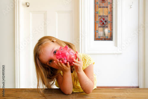 young girl wearing yellow blouse holding a pink piggy bank photo