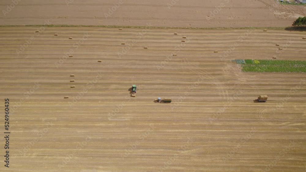 Aerial View Of Working Tractors On A Field With Baler And Trailer During Harvest Season. Aerial View Of Working Tractors On A Field With Baler And Trailer During Harvest Season.