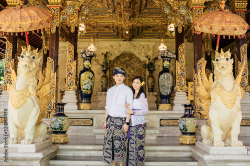 Couple in love in front of a temple. Both are wearing traditional clothes from Bali that were udeng , kamen, and kebaya.  photo