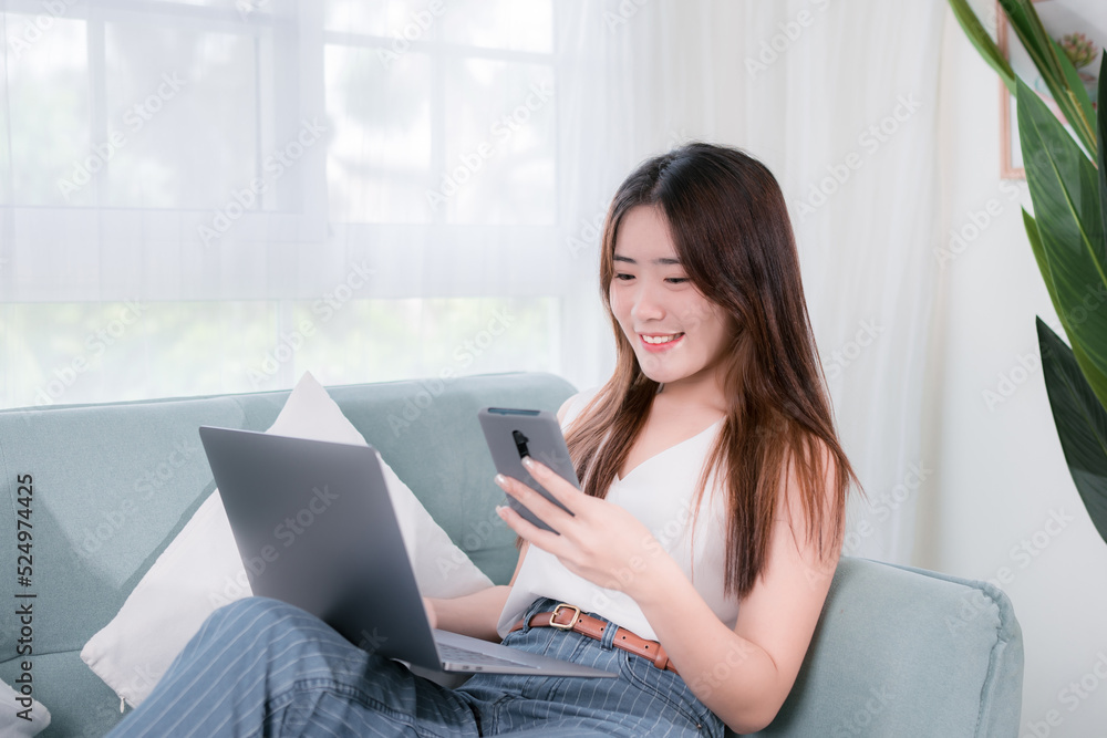 Asian woman use laptop and smartphone her enjoy and fun sitting on sofa in living room at home Asian woman use laptop and smartphone her enjoy and fun sitting on sofa in living room at home