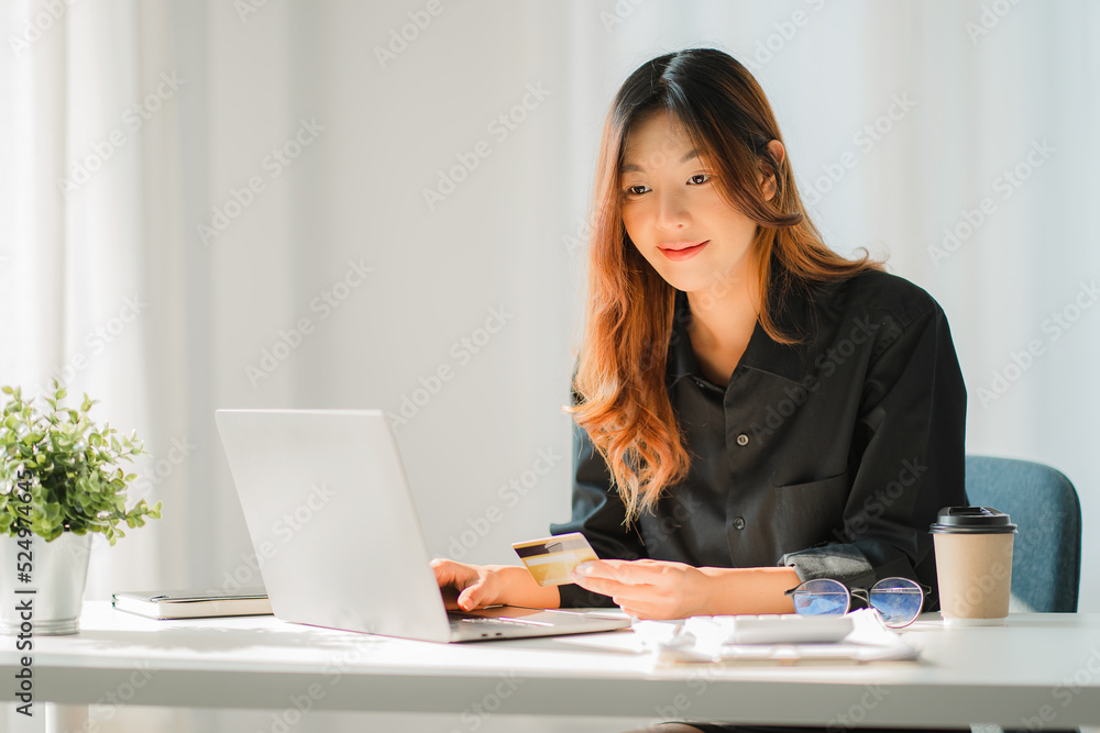 Asian woman holding credit card and using laptop online shopping concept. Easier shopping and credit card payment at office desk.