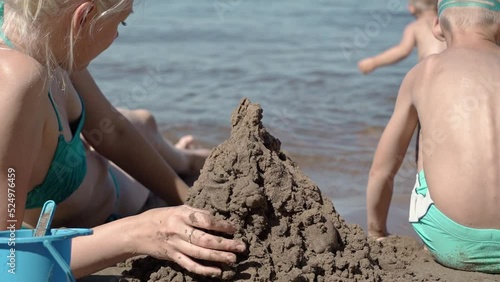 The mother of two sons came to the beach on this hot summer day. Children are busy with their own interests. One builds sand figures, the other splashes in the water. The woman helps them. photo