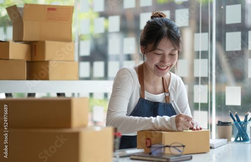 Asian female entrepreneurs and online sales. Woman is self-employed, working at home with a small business owner. Packaging delivery and SME online marketing © wichayada