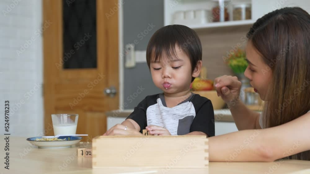 Asian young mother is taking her cute little son to play with toys while eating in the kitchen at house. Asian young mother is taking her cute little son to play with toys while eating in the kitchen at house.