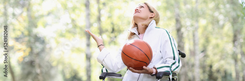 Young woman sitting in wheelchair holding basketball in park