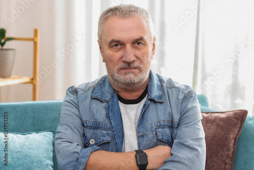 Фотография Angry senior man with gray hair and crossed arms looking at camera, sitting on s