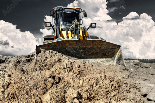 Powerful bulldozer or loader moves the earth at the construction site against the sky. An earthmoving machine is leveling the site. Construction heavy equipment for earthworks. photo