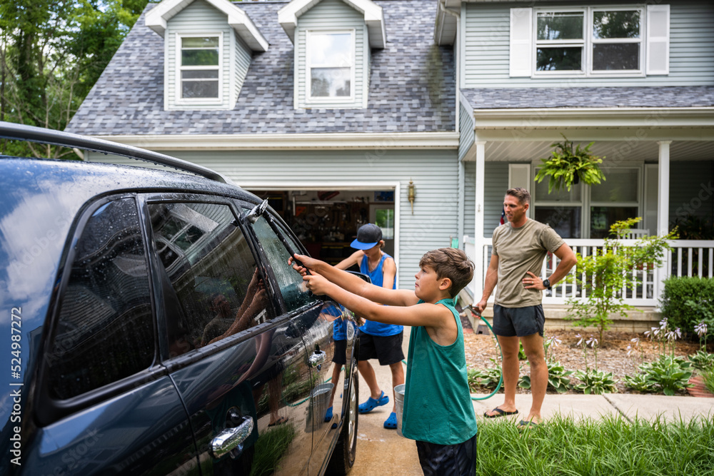 Obraz premium Air Force service member washes his vehicles with his sons in the driveway.