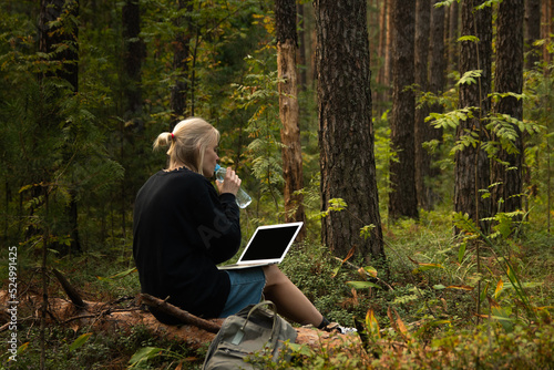 a young freelance girl is working on a laptop in the woods. remote work in nature