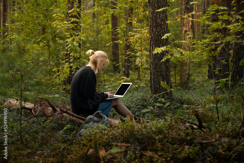 a young freelance girl is working on a laptop in the woods. remote work in nature