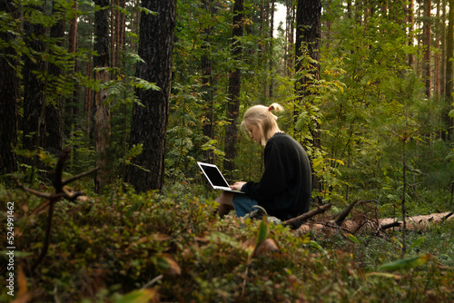 a young freelance girl is working on a laptop in the woods. remote work in nature