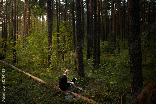 a young freelance girl is working on a laptop in the woods. remote work in nature