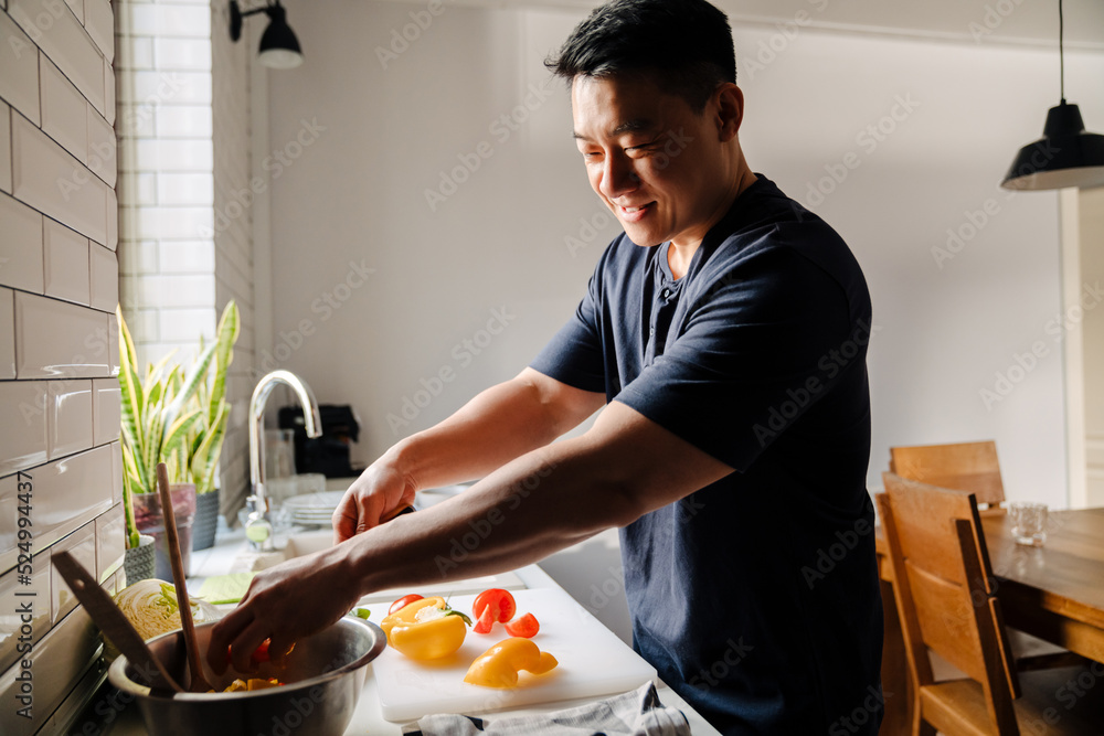 Adult happy smiling asian man cutting vegetables and cooking