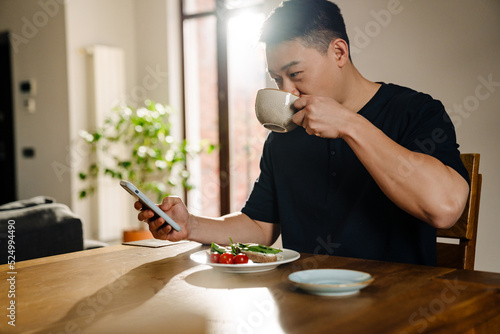 Adult asian man with phone drinking tea at lunch