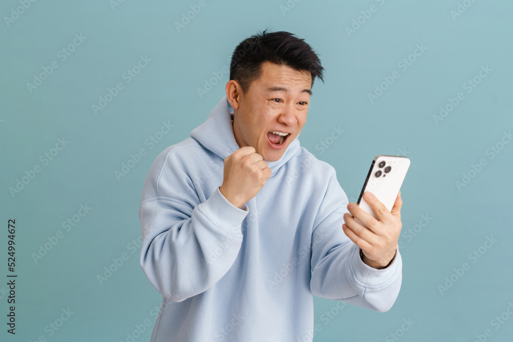 Happy brunette asian adult man rejoicing while looking at cellphone Happy brunette asian adult man rejoicing while looking at cellphone