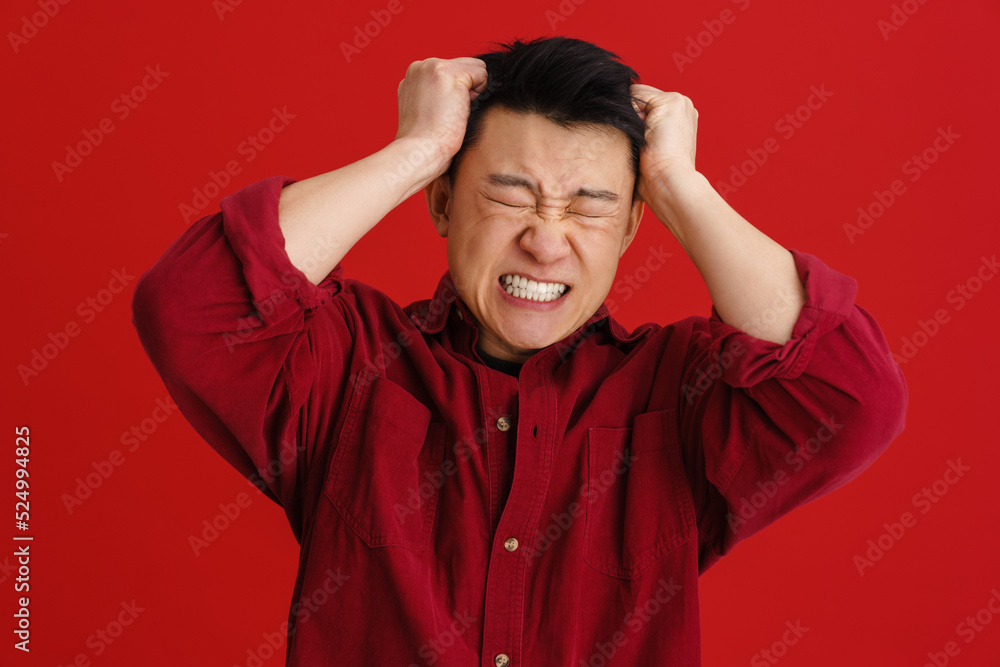 Asian man with headache grimacing while holding his head Asian man with headache grimacing while holding his head