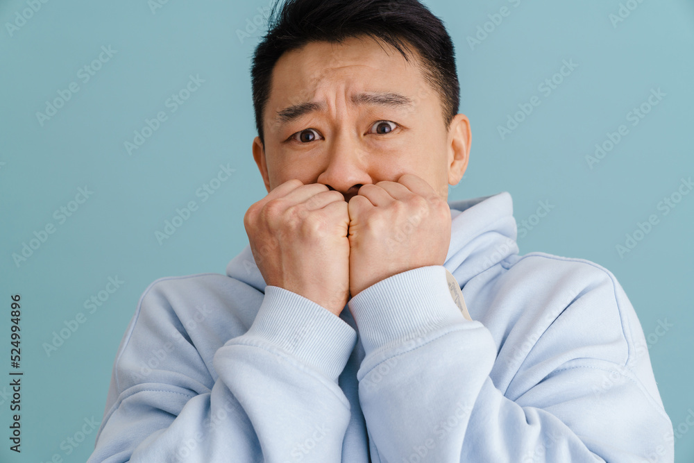 Brunette adult asian scared man covering his mouth with fists Brunette adult asian scared man covering his mouth with fists
