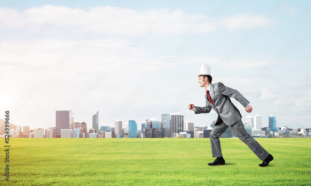 King businessman in elegant suit running on green grass and modern cityscape at background