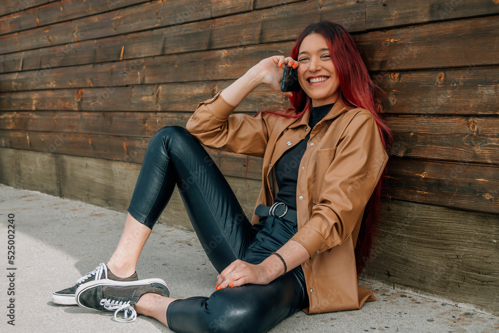 young woman with beige leather jacket at the wall with mobile phone young woman with beige leather jacket at the wall with mobile phone
