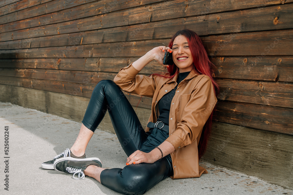 redhead smiling young girl in beige leather jacket at wall with mobile phone redhead smiling young girl in beige leather jacket at wall with mobile phone
